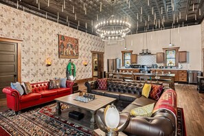 Un salon spacieux avec un canapé rouge, un canapé en cuir marron et une table basse. Un lustre est suspendu au plafond et un tableau orne le mur.