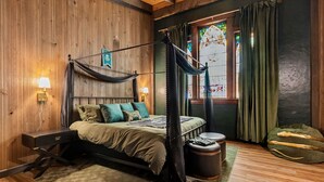 Ein gemütliches Schlafzimmer mit Himmelsbett, Holzboden, gepolstertem grünen Sitzbank und einem farbigen Glasfenster.