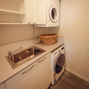 A laundry area with a washing machine, a sink, and a wicker basket on the countertop. - Sjøro • Stunning Sea Views • Beach Access • Sauna (Kingston Beach)