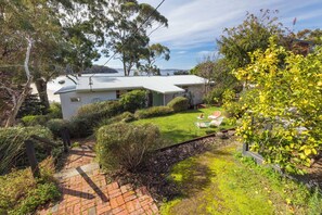 A residential property with a paved driveway leading to a house with a metal roof, surrounded by lush greenery and a view of the sea. - Sjøro • Stunning Sea Views • Beach Access • Sauna (Kingston Beach)