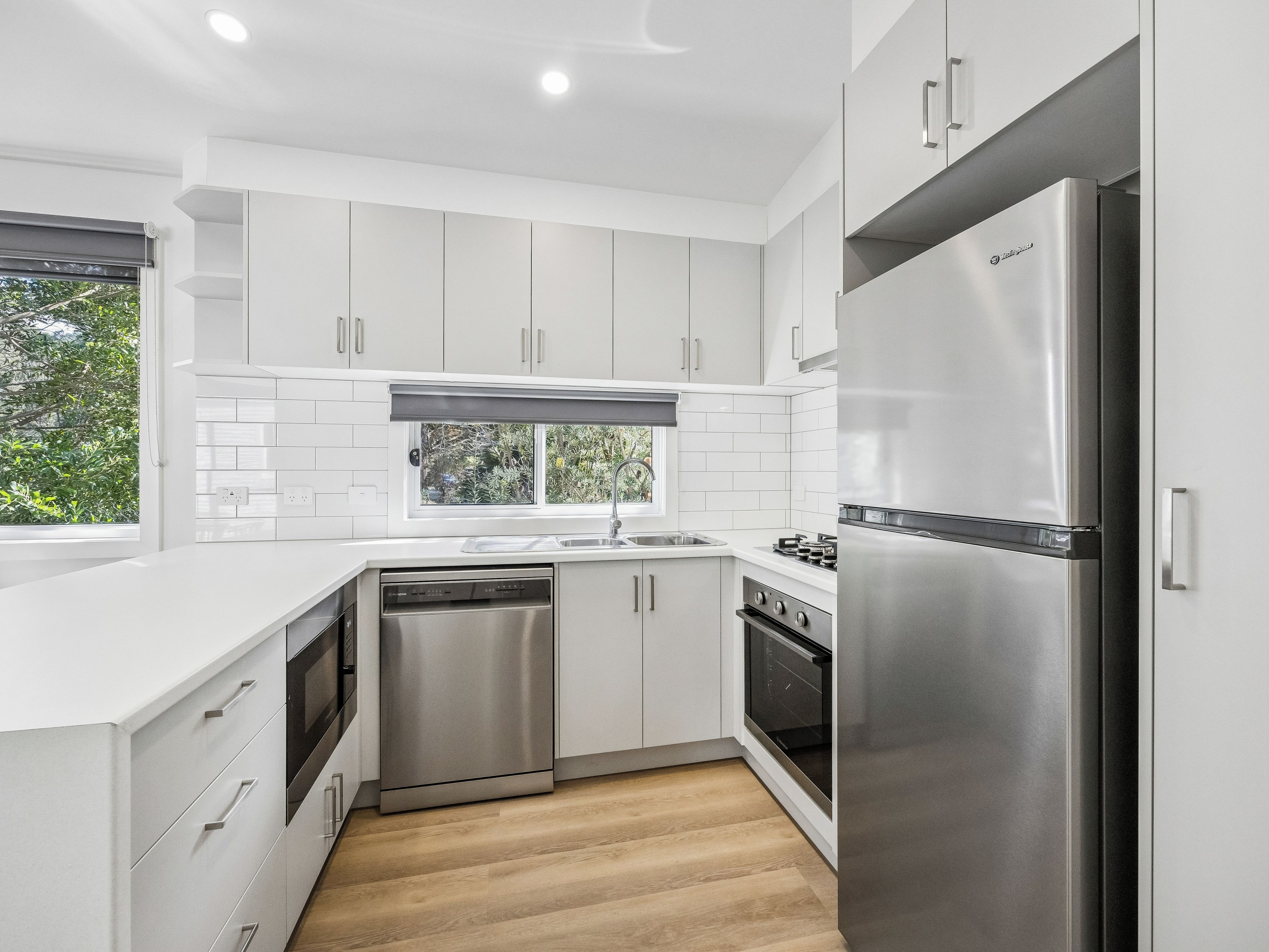 A modern kitchen with white cabinetry, stainless steel appliances, and a window providing natural light.