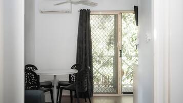 A room with a ceiling fan, a window with a metal screen, a white table with four chairs, and a wooden floor.