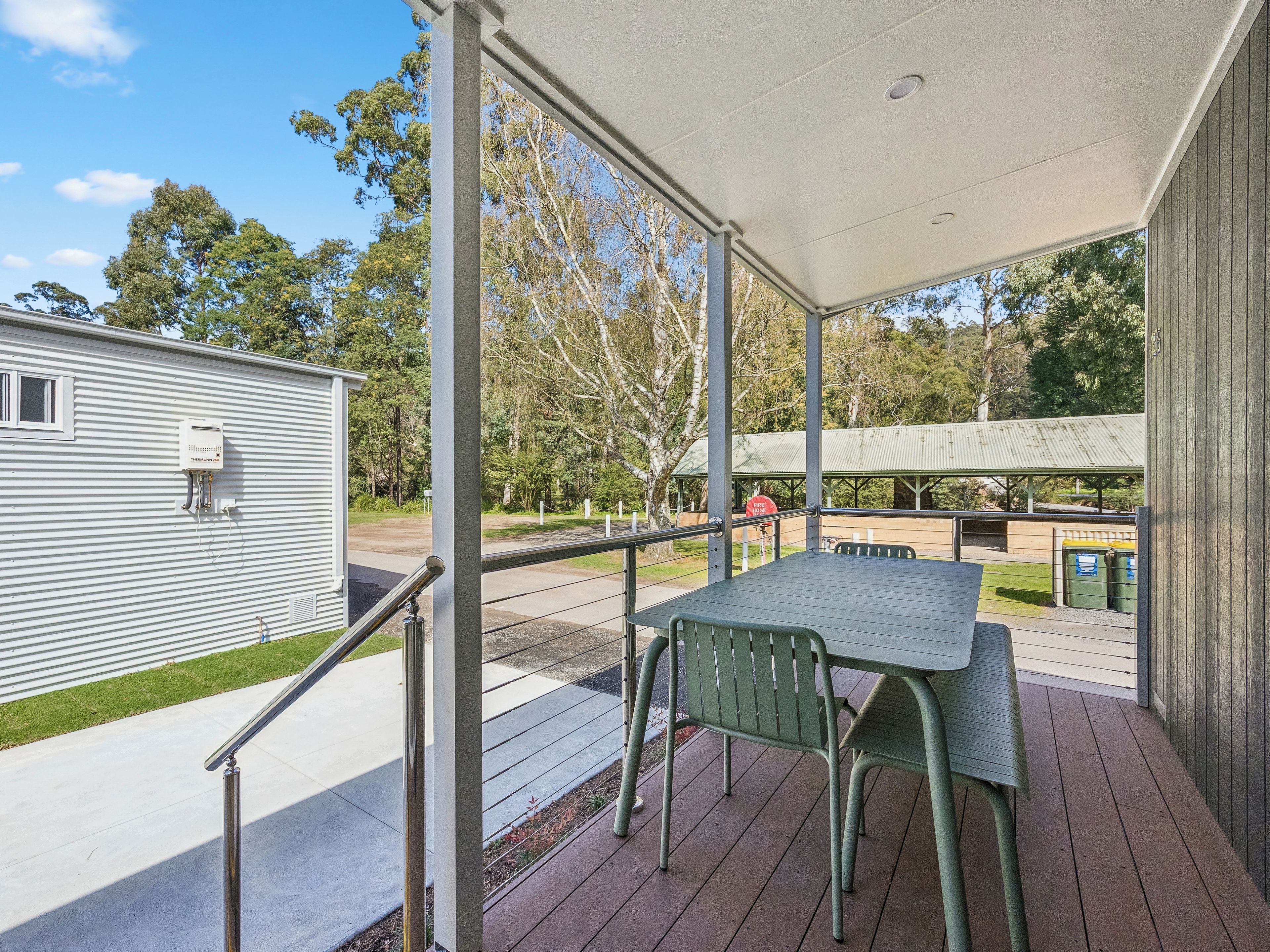 A covered outdoor area with a table and chairs, a metal railing, and a view of a building and trees.