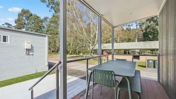A covered outdoor area with a table and chairs, a metal railing, and a view of a building and trees.