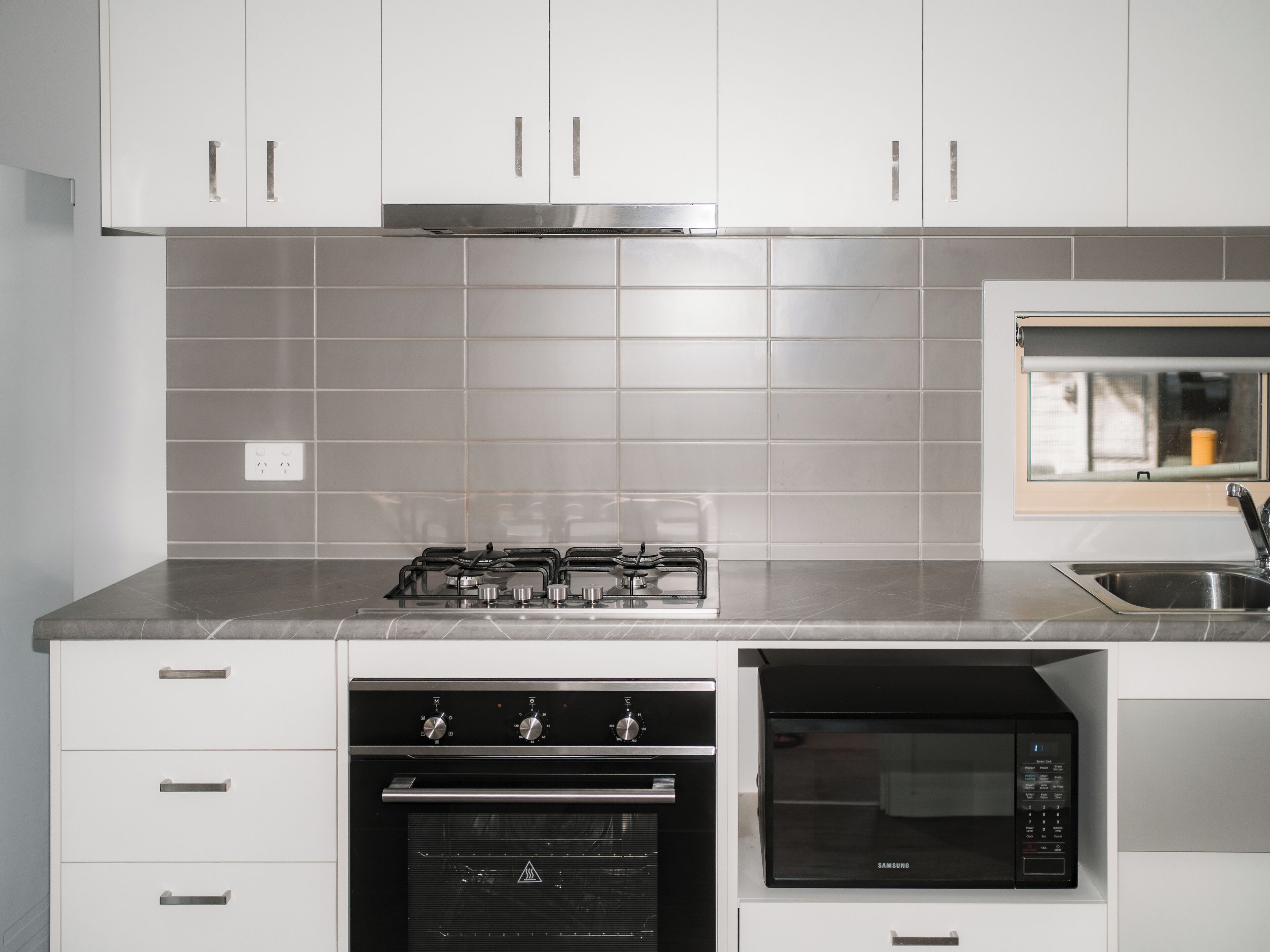 A kitchen with white cabinets, a gas stove, an oven, a microwave, and a window above the sink.