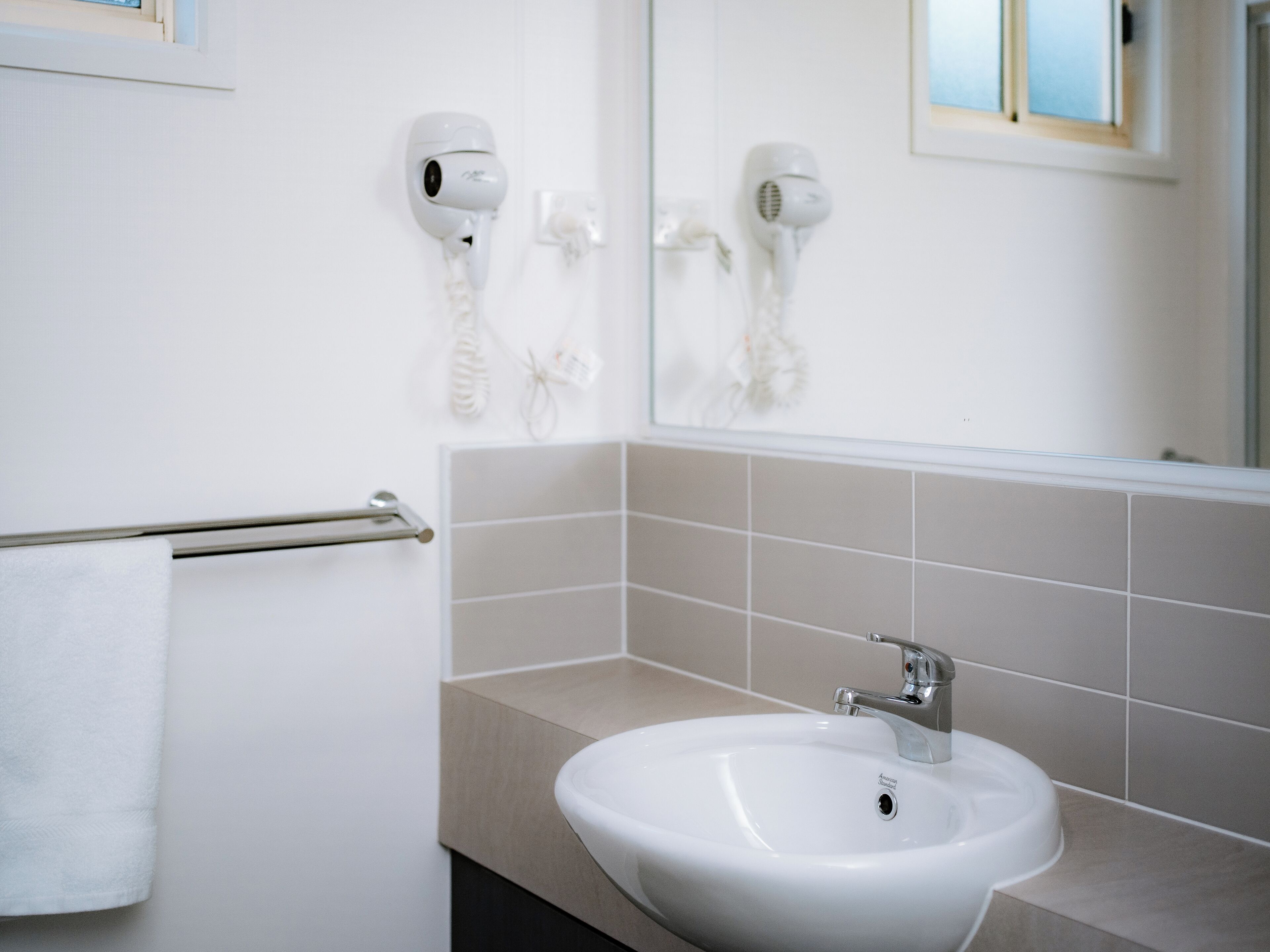 Ein Badezimmer mit einem weißen Waschbecken, einem Handtuchhalter und zwei an der Wand befestigten Haartrocknern.