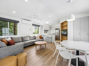 A modern kitchen with white cabinets, a stainless steel refrigerator, and a dining area with a white table and chairs. - Warburton Holiday Park (Warburton)