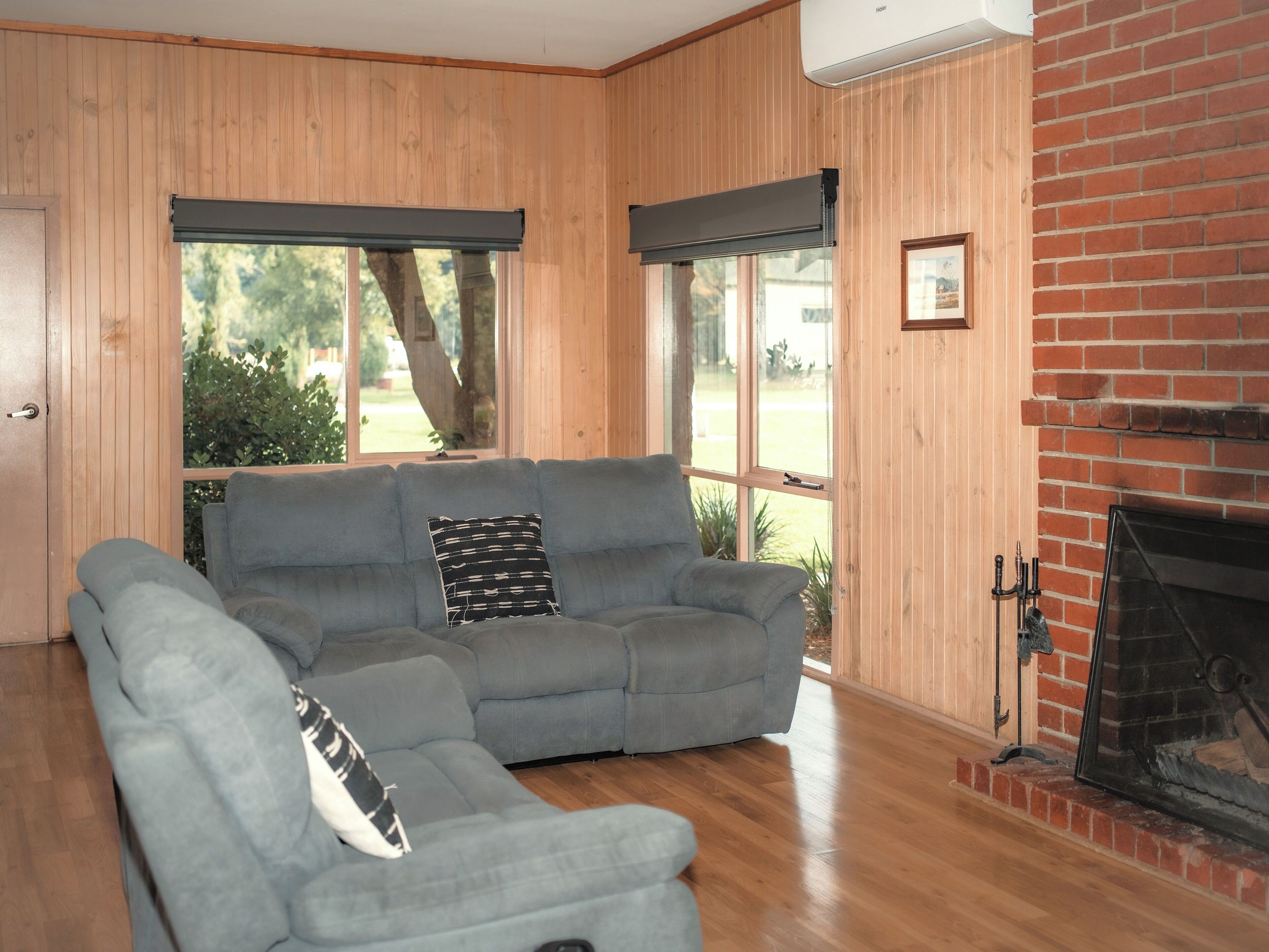 Una habitación con un sofá seccional gris, una chimenea y ventanas amplias con persianas.