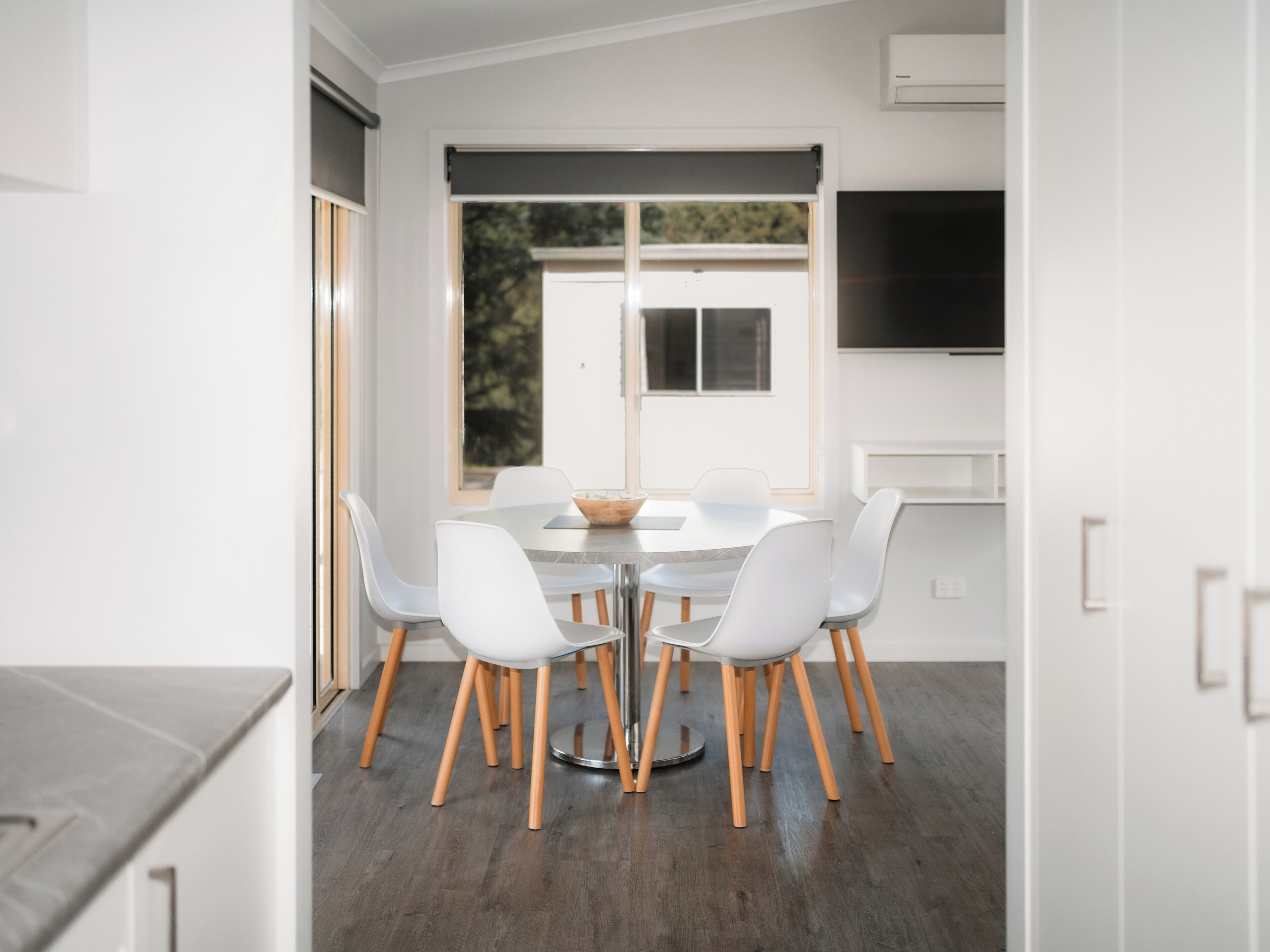Een moderne eethoek met een ronde tafel, witte stoelen en uitzicht op het landschap door een groot raam.