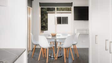 Een moderne eethoek met een ronde tafel, witte stoelen en uitzicht op het landschap door een groot raam.