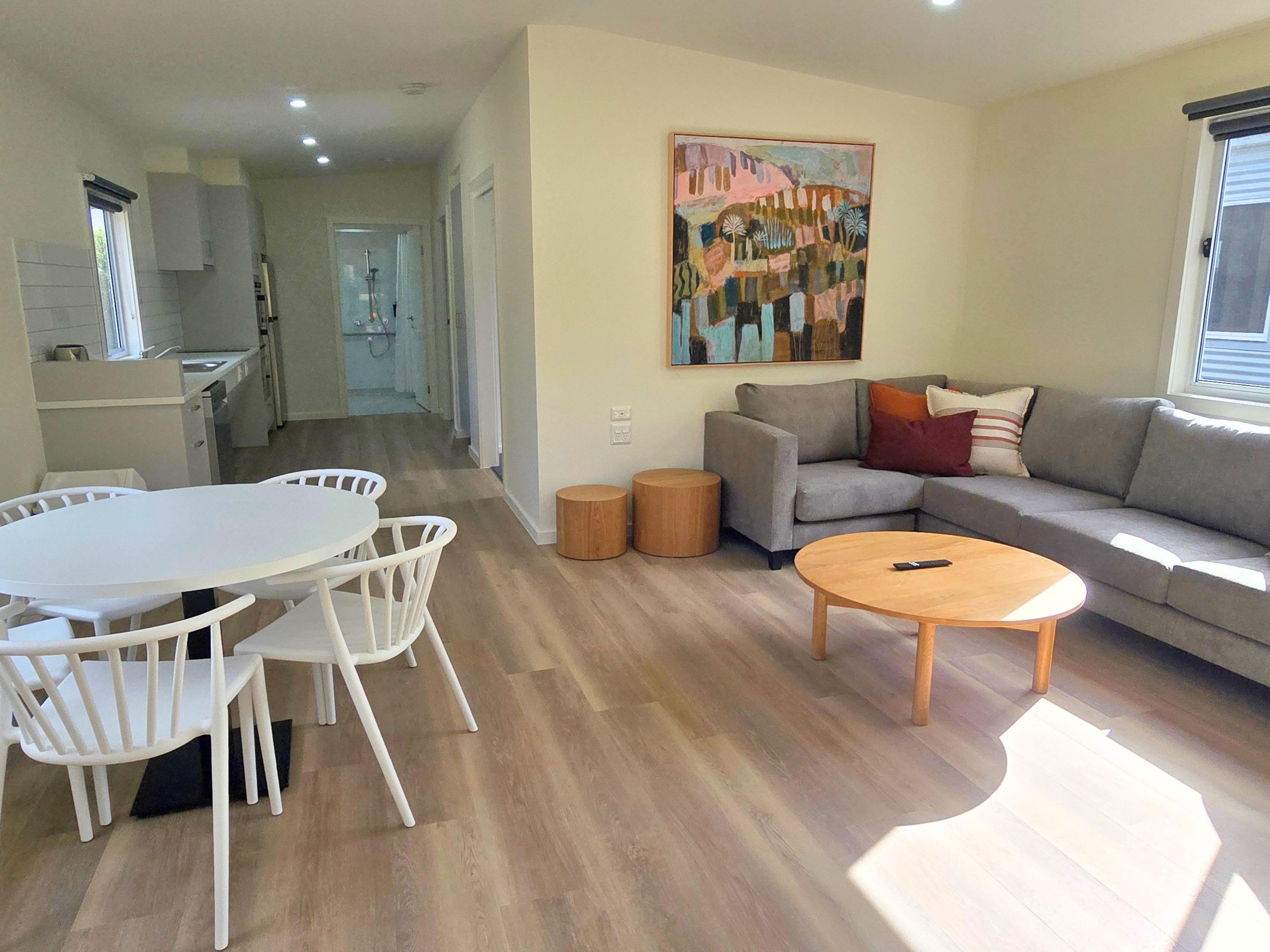 A modern living room with a grey sofa, a round wooden coffee table, and a dining area with a white table and chairs.
