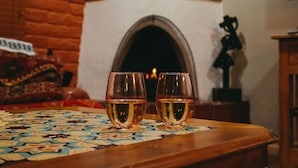 Two glasses of amber liquid on a table with a patterned tablecloth, a brick wall, and a fireplace in the background. - Art-Filled Casita, Walk to Plaza, Hottub & Pool (Santa Fe)
