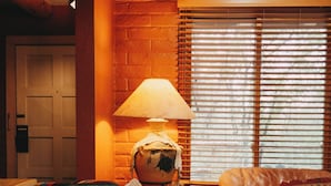 A cozy living room with a leather sofa, patterned cushions, a lamp, and a window with blinds. - Art-Filled Casita, Walk to Plaza, Hottub & Pool (Santa Fe)