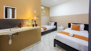 Quarto de hotel com banheiro, duas camas, mesa de cabeceira e criado-mudo.