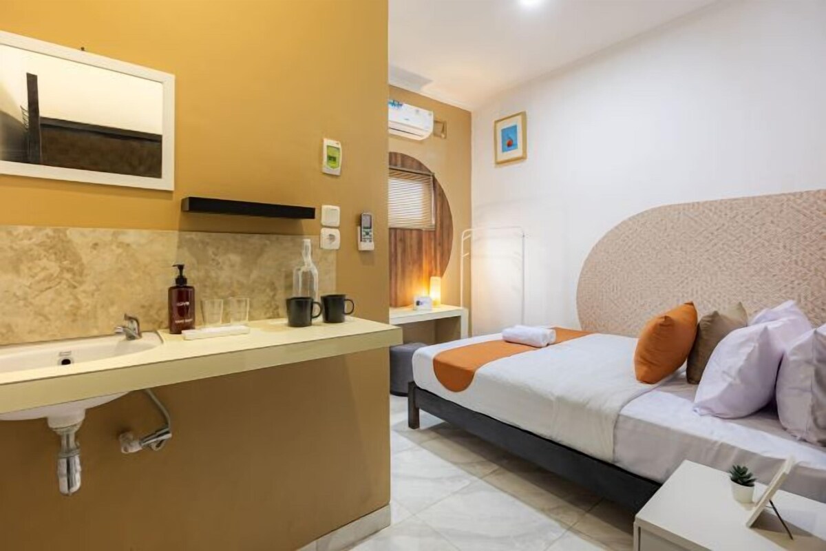 A hotel room with a bed, bedside table, and a bathroom with a sink and mirror.