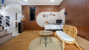 Um interior moderno com piso de madeira, um tapete redondo trançado, uma cadeira de vime, uma escrivaninha branca com um computador e uma escada.