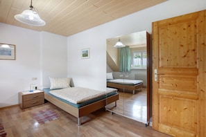 Une chambre avec un plafond en bois, un lit avec un matelas vert, une table de chevet, un miroir et une porte en bois.