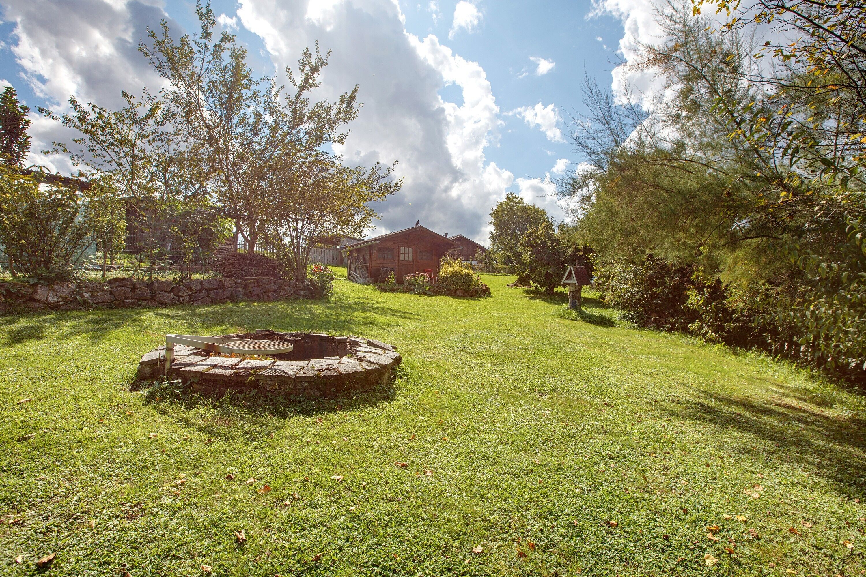 A backyard with a stone fire pit, a wooden deck, and a house in the background.