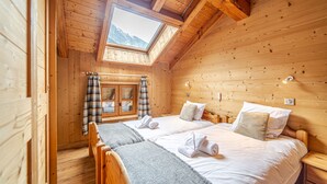 Een houten kamer met twee bedden, dakraam en uitzicht op bergen.