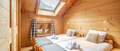 Habitación de cabaña de madera con dos camas, tragaluz y vistas a las montañas.