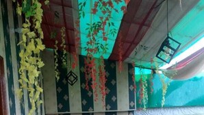 A room with a wooden floor, striped wallpaper, and hanging floral decorations. - New View Inn (Varanasi)