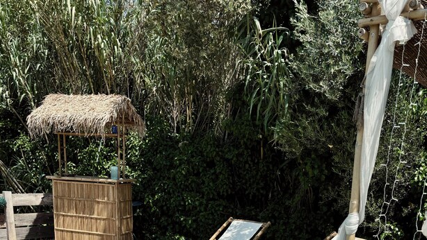 Eine Holzterrasse mit Pool, einer Holzbank, einer Strohhütte und einem weißen Baldachin.