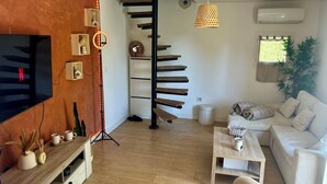 Ein modernes Wohnzimmer mit Fernseher, Couchtisch aus Holz, weißes Sofa und einer Holztreppe.