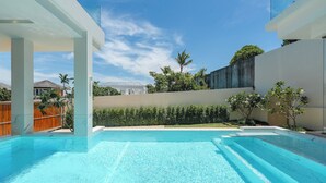 Una piscina exterior moderna con agua azul cristalina, rodeada por un diseño arquitectónico minimalista, una valla de madera y exuberante vegetación.