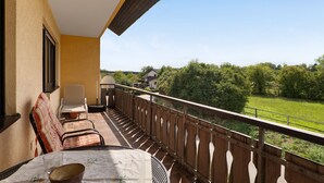 A balcony with a table, chairs, and a view of a green landscape.