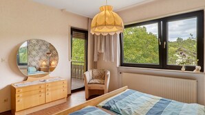 A bedroom with a bed, a dresser, a chair, a large window with a view, and a hanging light fixture.