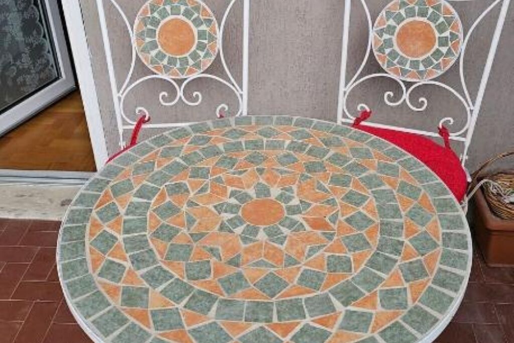A circular mosaic floor with a geometric pattern, a metal railing with a red cushion, and a brown wall in the background.