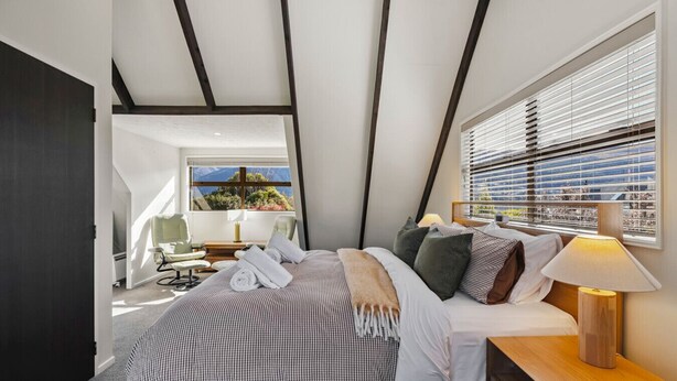 Une chambre à coucher moderne avec un grand lit, une table de chevet avec une lampe et une vue sur l’extérieur par la fenêtre.