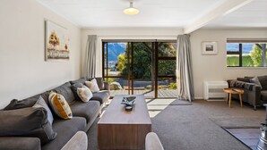 Un salon moderne avec un canapé, une table basse et une vue sur les montagnes, visible à travers de grandes portes vitrées.