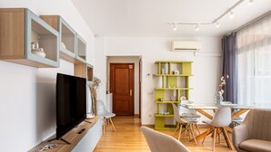 A modern living room with a flat-screen TV, wooden cabinets, a dining area with a glass table, and a sofa.