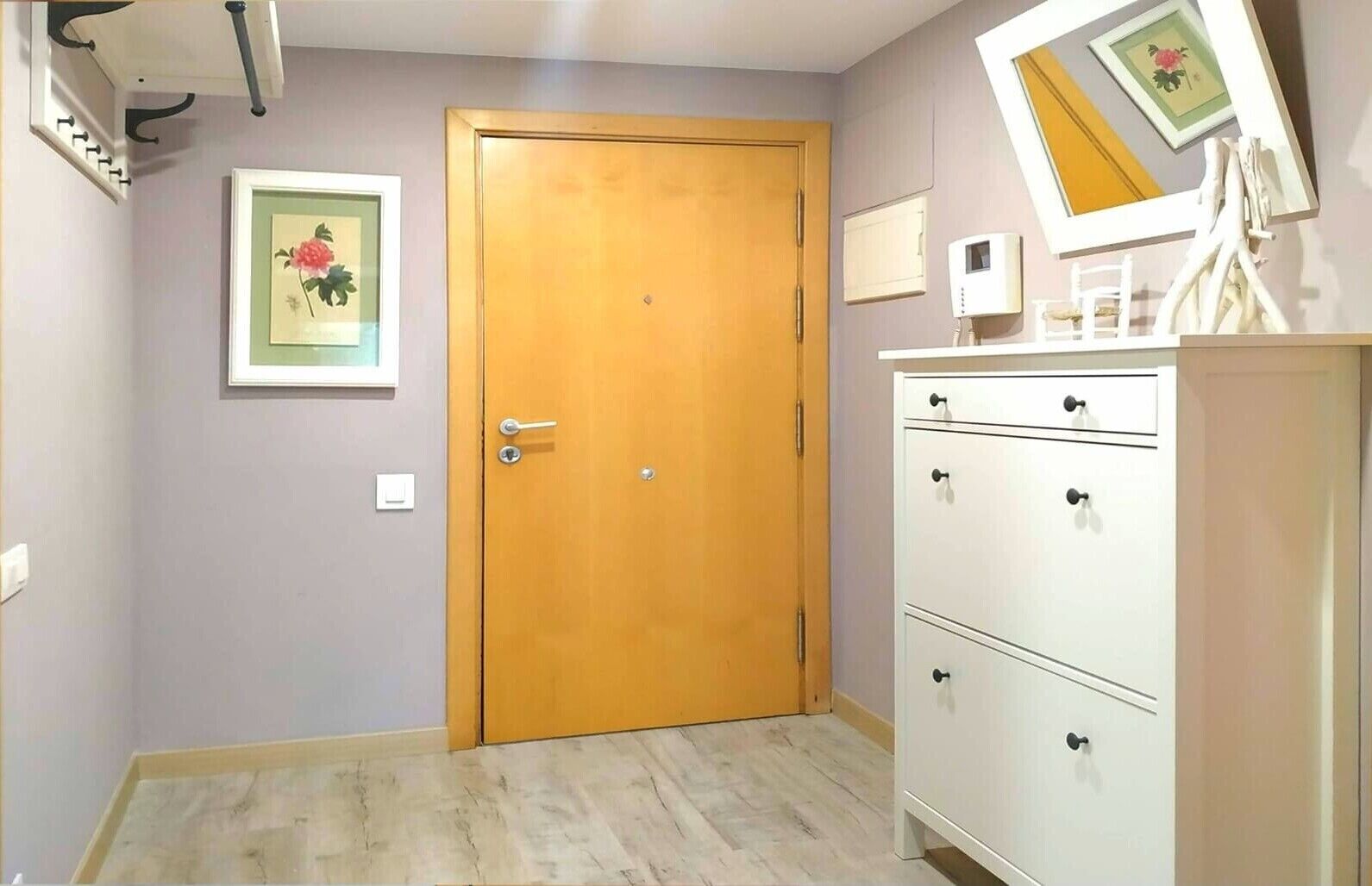 Een kamer met een houten deur, een witte dressoir, een lijst met een afbeelding aan de muur en een thermostaat.