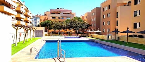 A swimming pool with a diving board, surrounded by apartment buildings and trees.