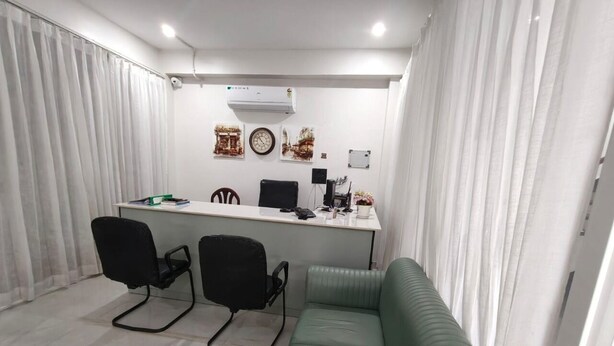 A modern office space with a desk, two black office chairs, a green sofa, and a white air conditioning unit on the wall. - Hotel YJ Manor (Dehradun)