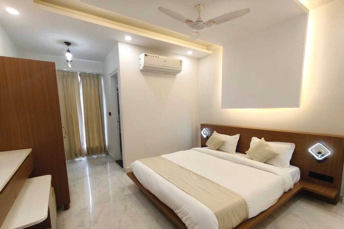 A modern hotel room with a large bed, wooden headboard, bedside tables, a ceiling fan, and an air conditioning unit.