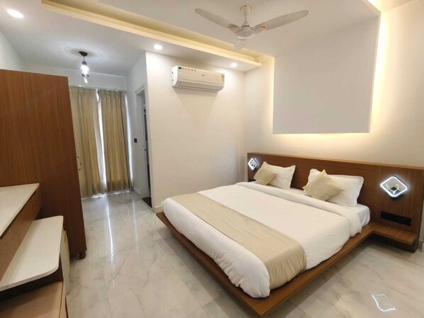 Una habitación de hotel moderna con una cama grande, cabecera de madera, mesitas de noche, ventilador de techo y unidad de aire acondicionado.