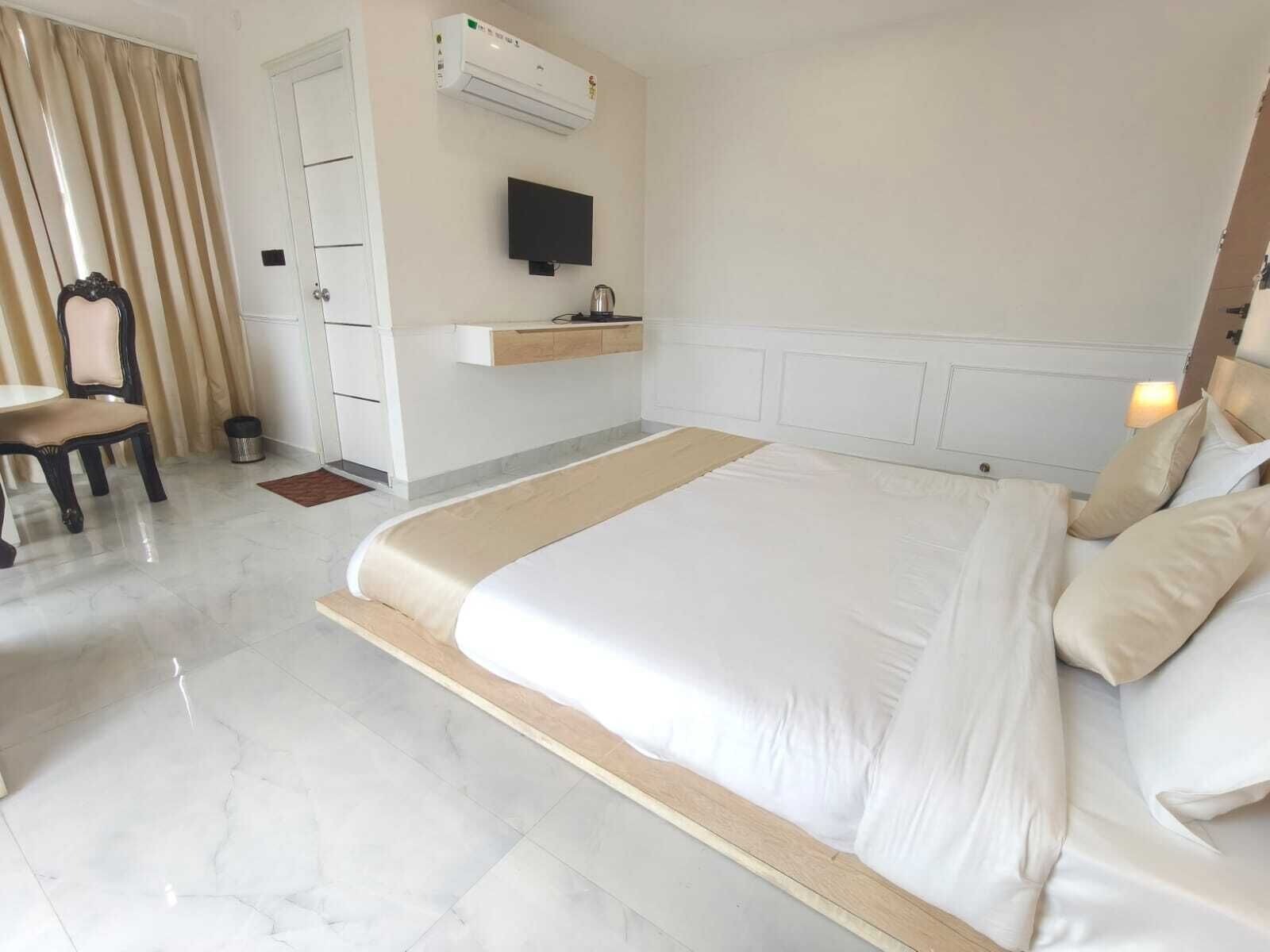 Ein Hotelzimmer mit einem großen Bett, einem an der Wand befestigten Fernseher, einem kleinen Waschbecken und einem Sessel.