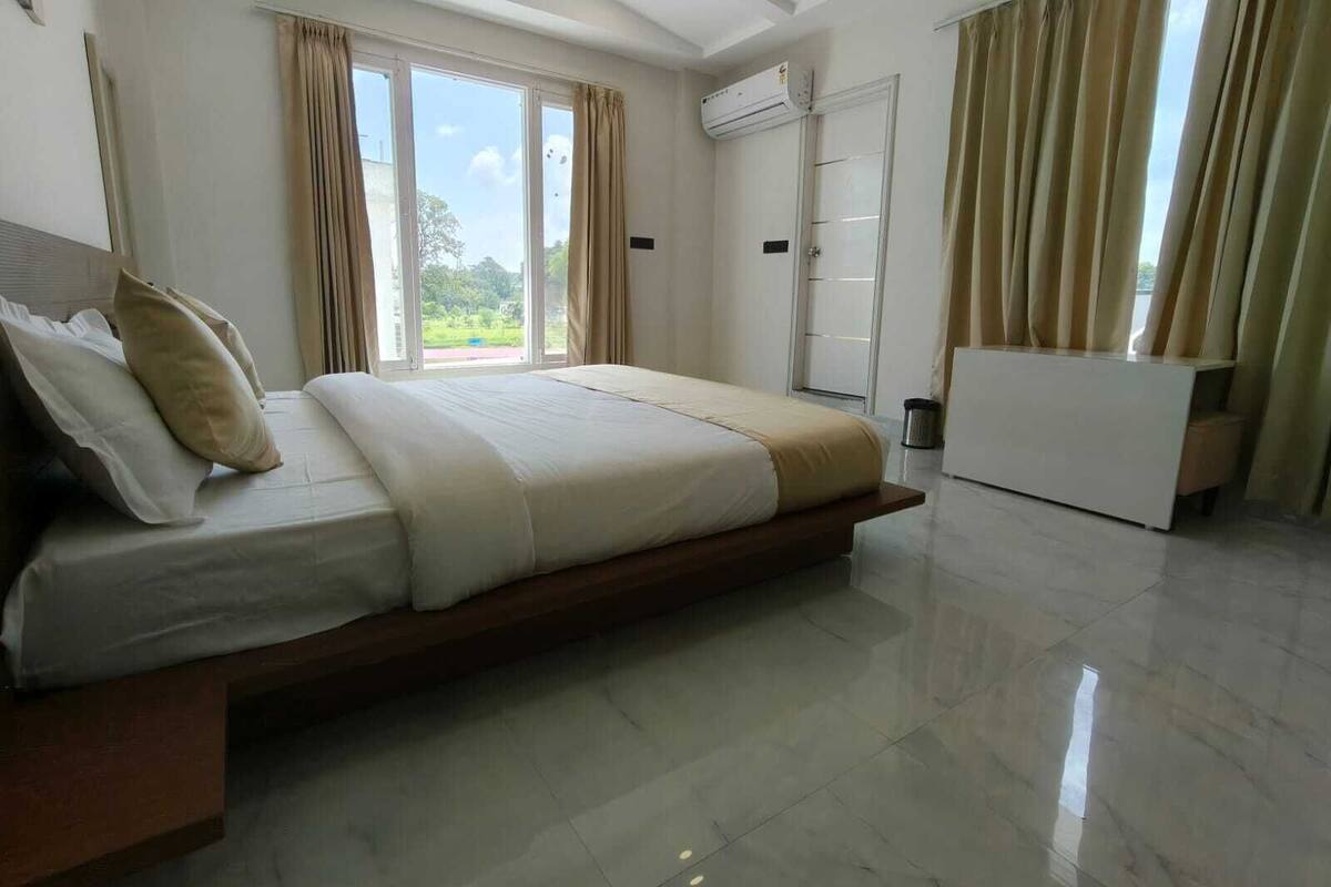A modern bedroom with a large bed, a built-in bench, a wardrobe, and a window with curtains.