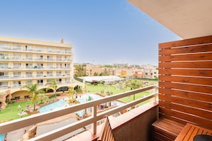 A hotel balcony with a view of a pool area, a multi-story building, and a clear sky.