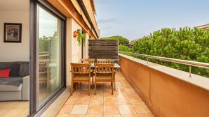Een balkon met een schuifdeur, een houten tafel met stoelen en uitzicht op een groen landschap.