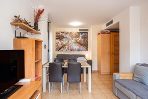 A compact living space with a dining area, a sofa, a TV, and a painting on the wall.