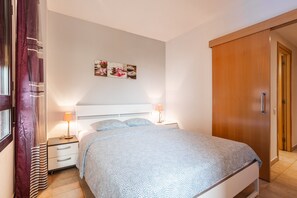 A bedroom with a bed, bedside tables, a nightstand, a wooden wardrobe, and a wall-mounted artwork.