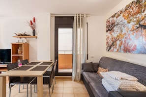 Una sala moderna con un sofá, una mesa de comedor con sillas, un televisor y un cuadro en la pared.