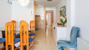 A modern kitchen with white cabinets, a wooden dining table with chairs, and a blue chair with a leaf pattern. - Apartment 'Verano Go2lloret' with Mountain View, Wi-Fi and Air Conditioning (Lloret de Mar)