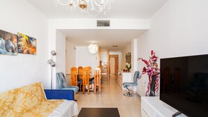 A living room with a sofa, TV, dining table, chairs, and a chandelier. - Apartment 'Verano Go2lloret' with Mountain View, Wi-Fi and Air Conditioning (Lloret de Mar)