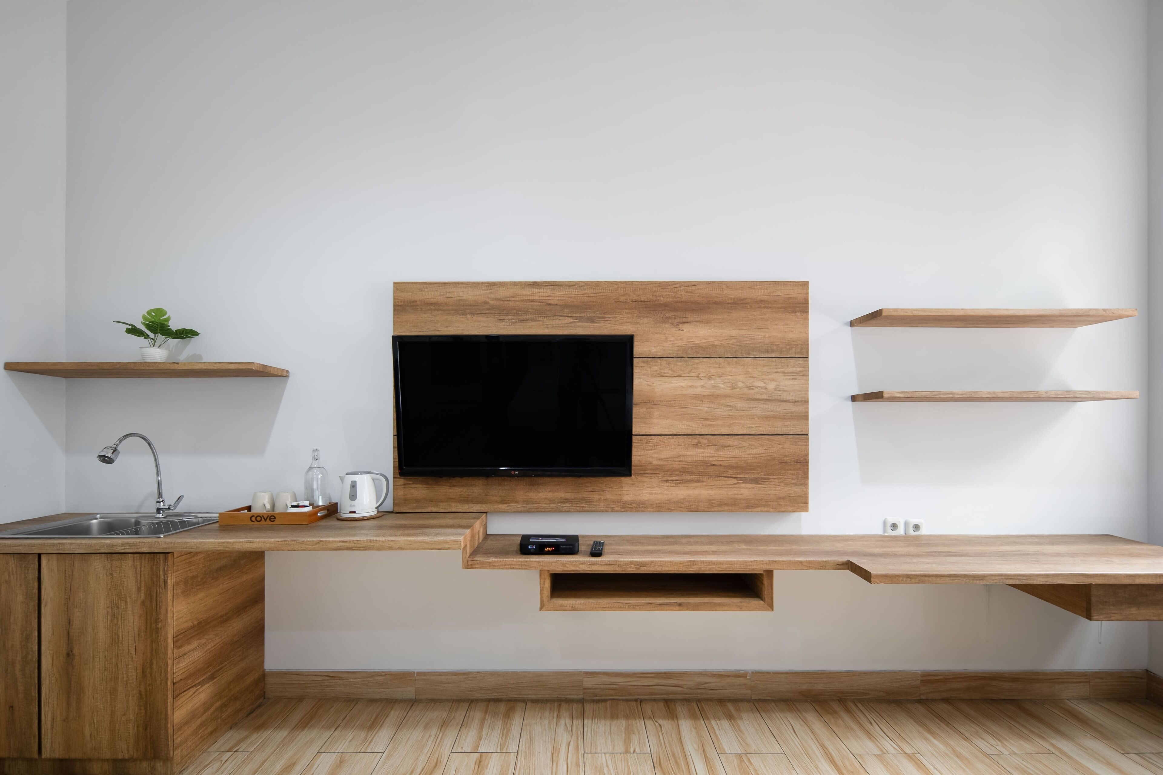 A modern kitchen with a built-in TV, wooden cabinetry, a sink, and a coffee maker.