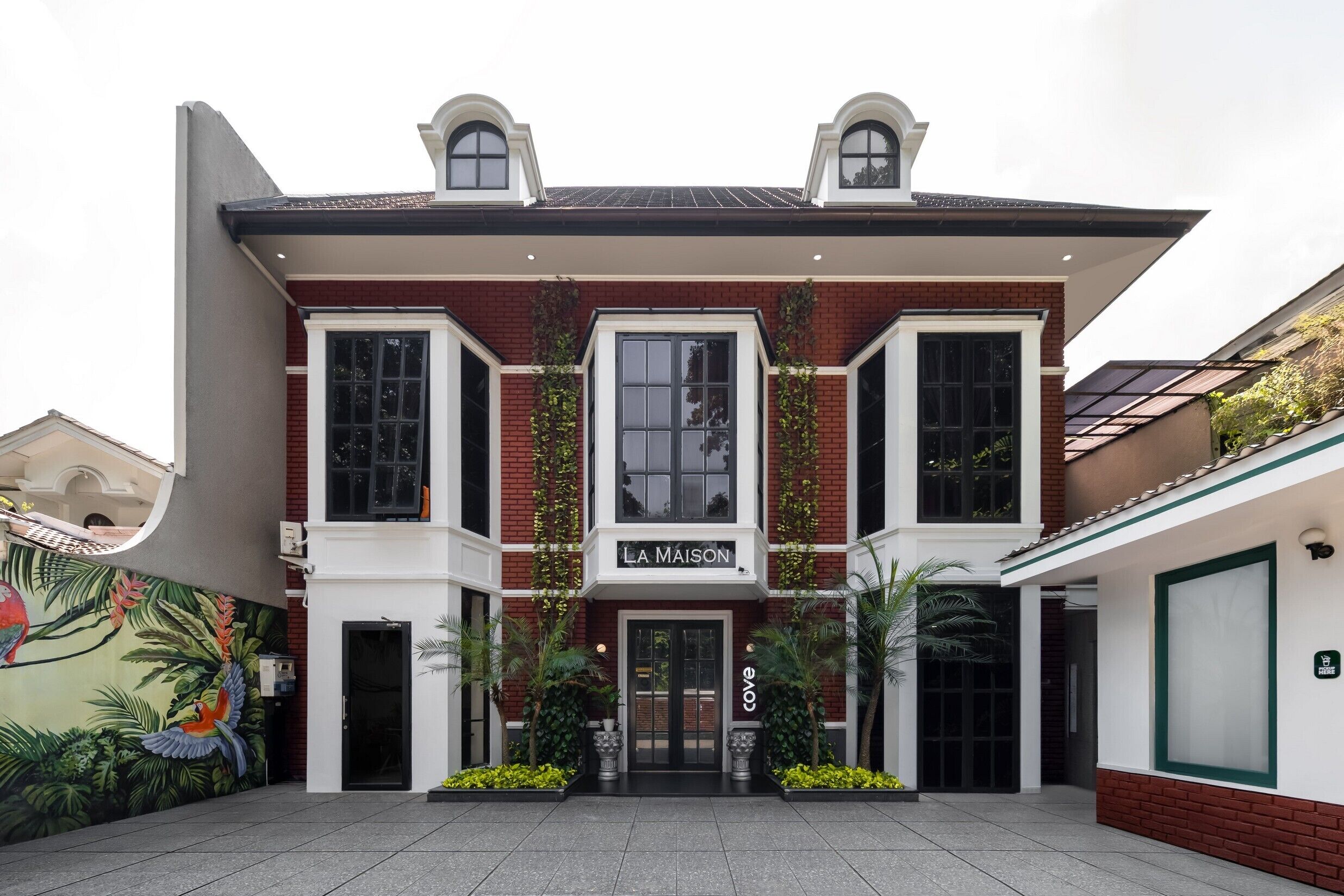 A two-story building with a sign reading "La Maison" and a mural of tropical birds on the left.